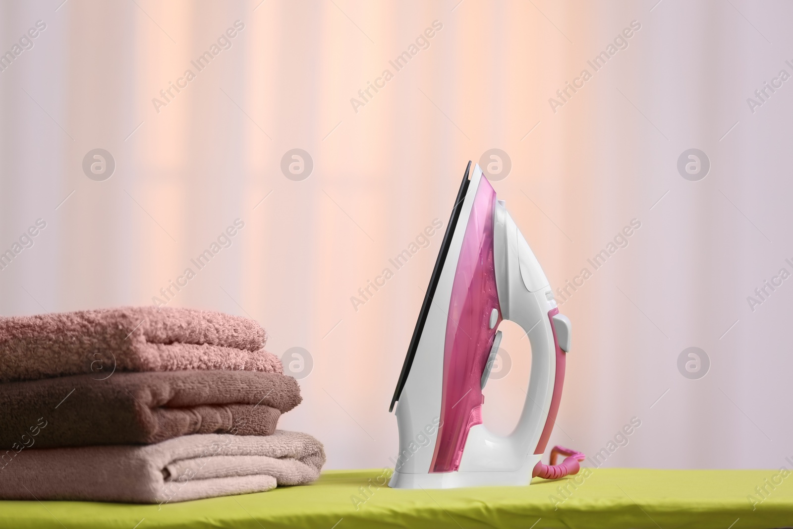 Photo of Modern iron and towels on board against blurred background