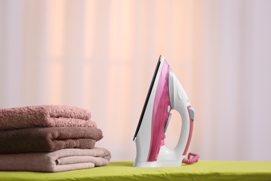 Modern iron and towels on board against blurred background