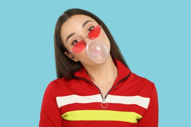 Beautiful young woman blowing bubble gum on light blue background