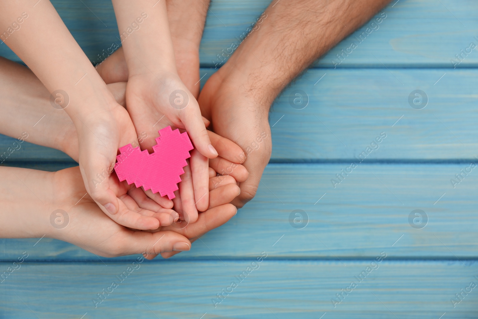 Photo of Top view of parents and kid holding pink heart in hands at turquoise wooden table, space for text. Family day