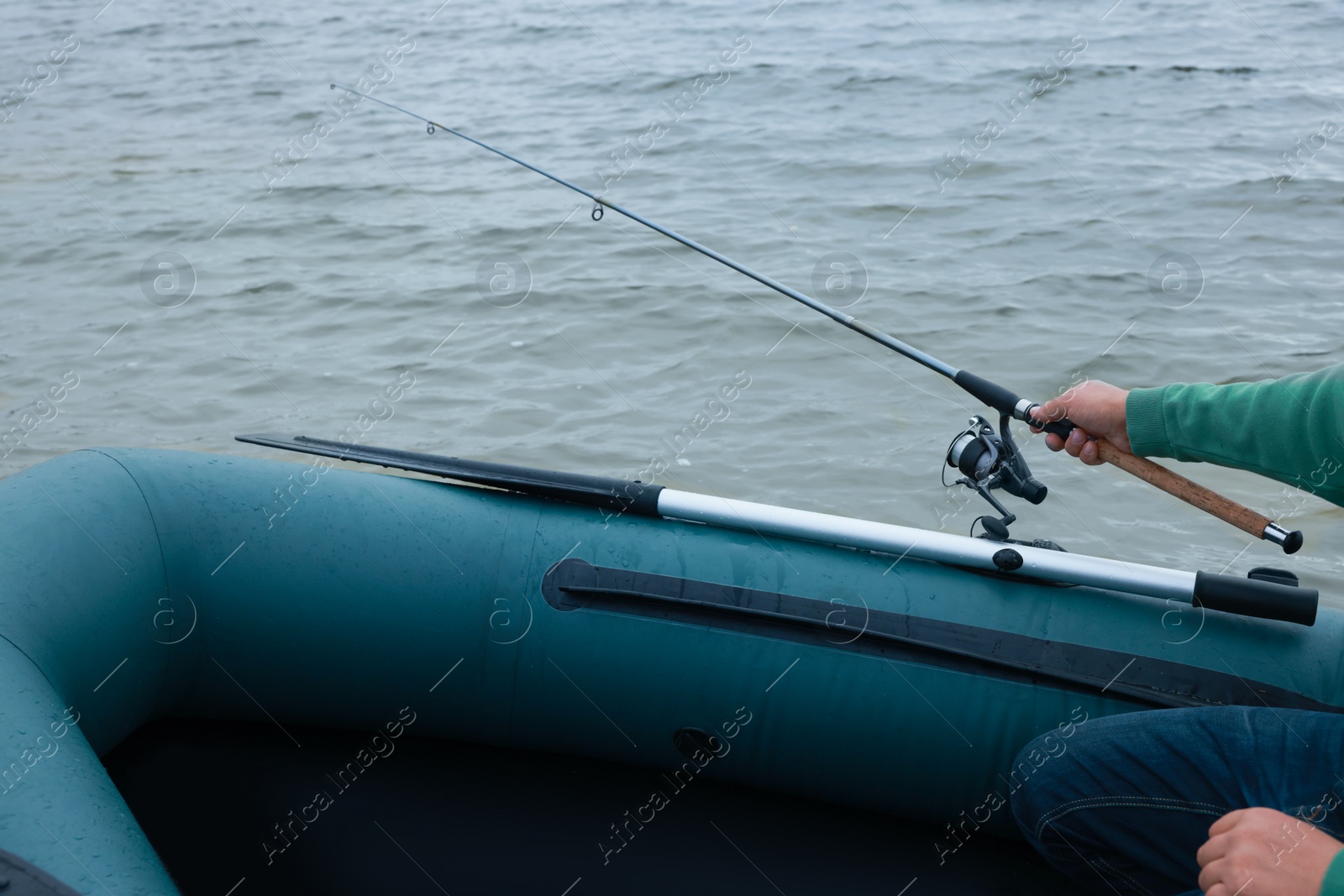 Photo of Man fishing with rod from inflatable rubber boat on river, closeup