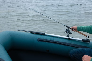 Photo of Man fishing with rod from inflatable rubber boat on river, closeup