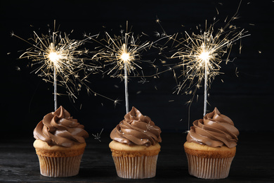 Image of Birthday cupcakes with sparklers on table against dark background