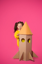 Little child playing with rocket made of cardboard box on pink background