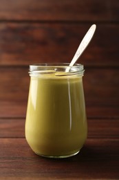 Tasty mustard sauce and spoon in glass jar on wooden table