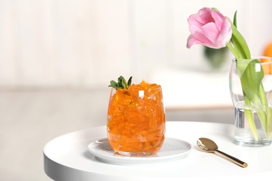 Glass of jelly and flower on table against blurred background