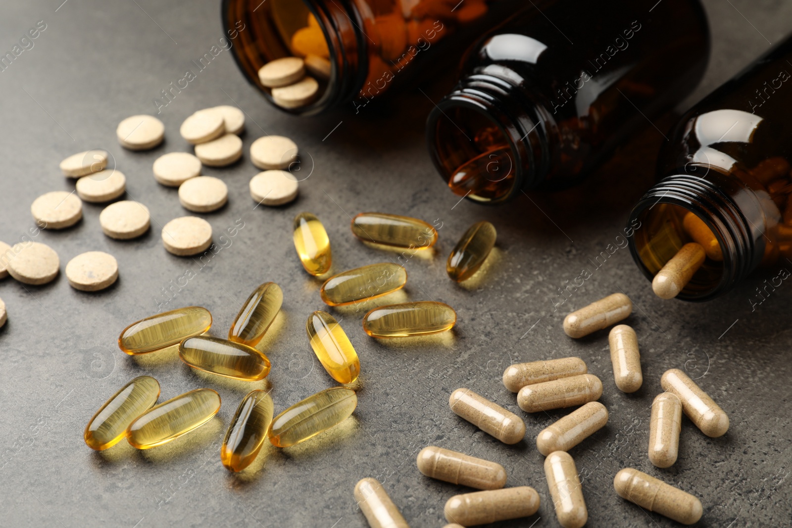 Photo of Overturned bottles with different dietary supplements on grey table, closeup