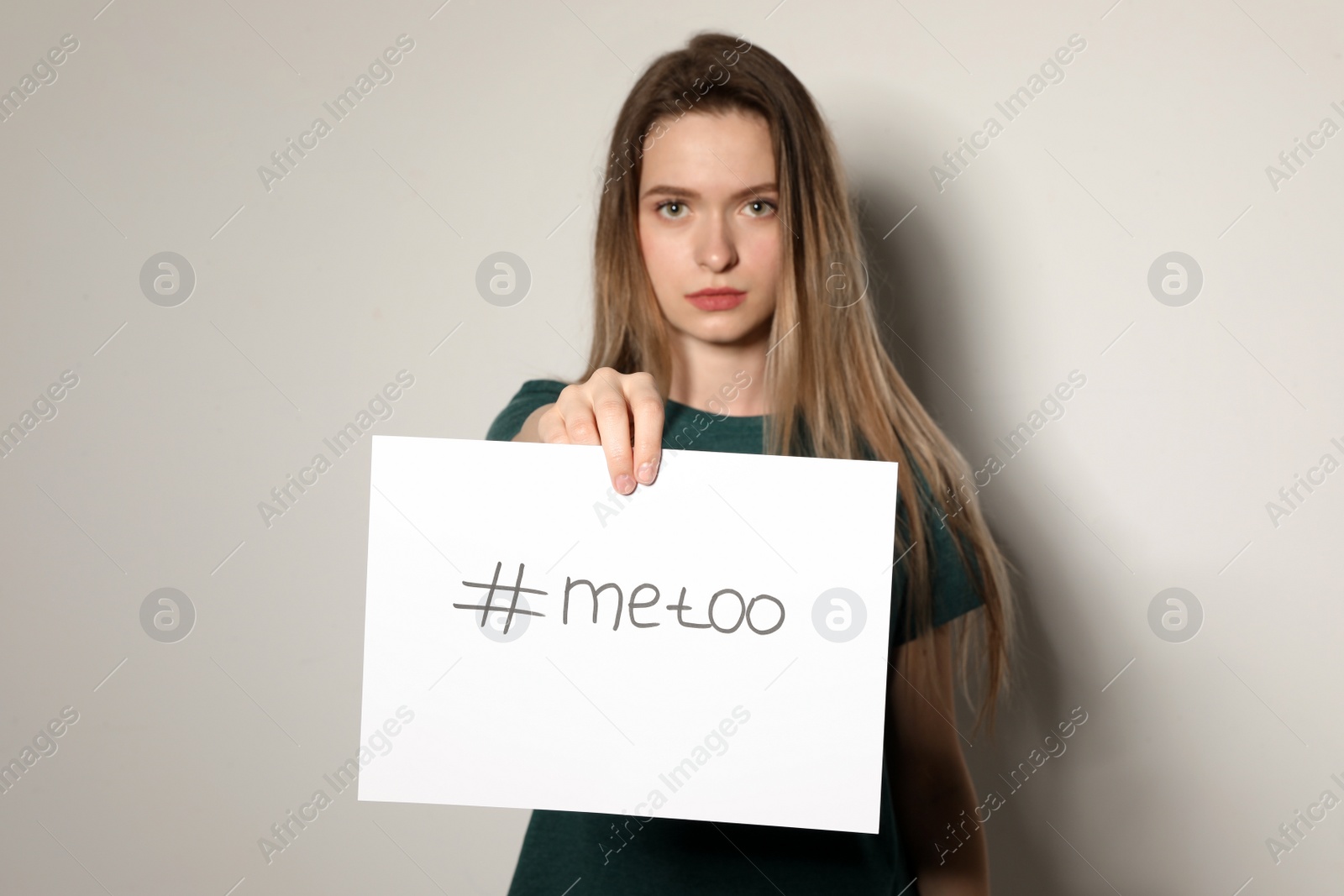 Photo of Young woman holding #METOO card against light background