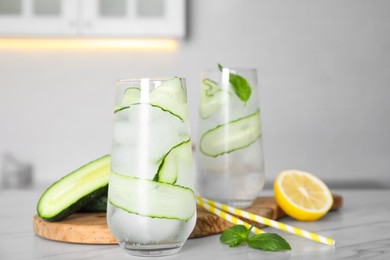 Photo of Tasty fresh cucumber water, sliced lemon and basil on white marble table indoors