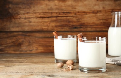 Photo of Milk with nutmegs and cinnamon on wooden table. Space for text