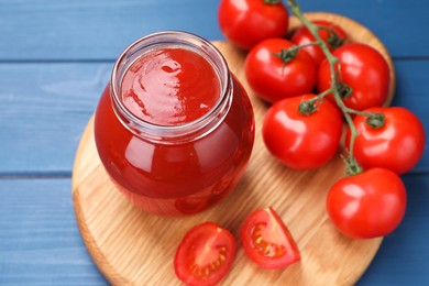 Organic ketchup in jar and fresh tomatoes on blue wooden table. Tomato sauce