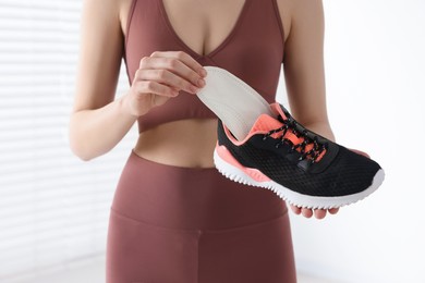Sporty woman putting orthopedic insole into shoe indoors, closeup. Foot care