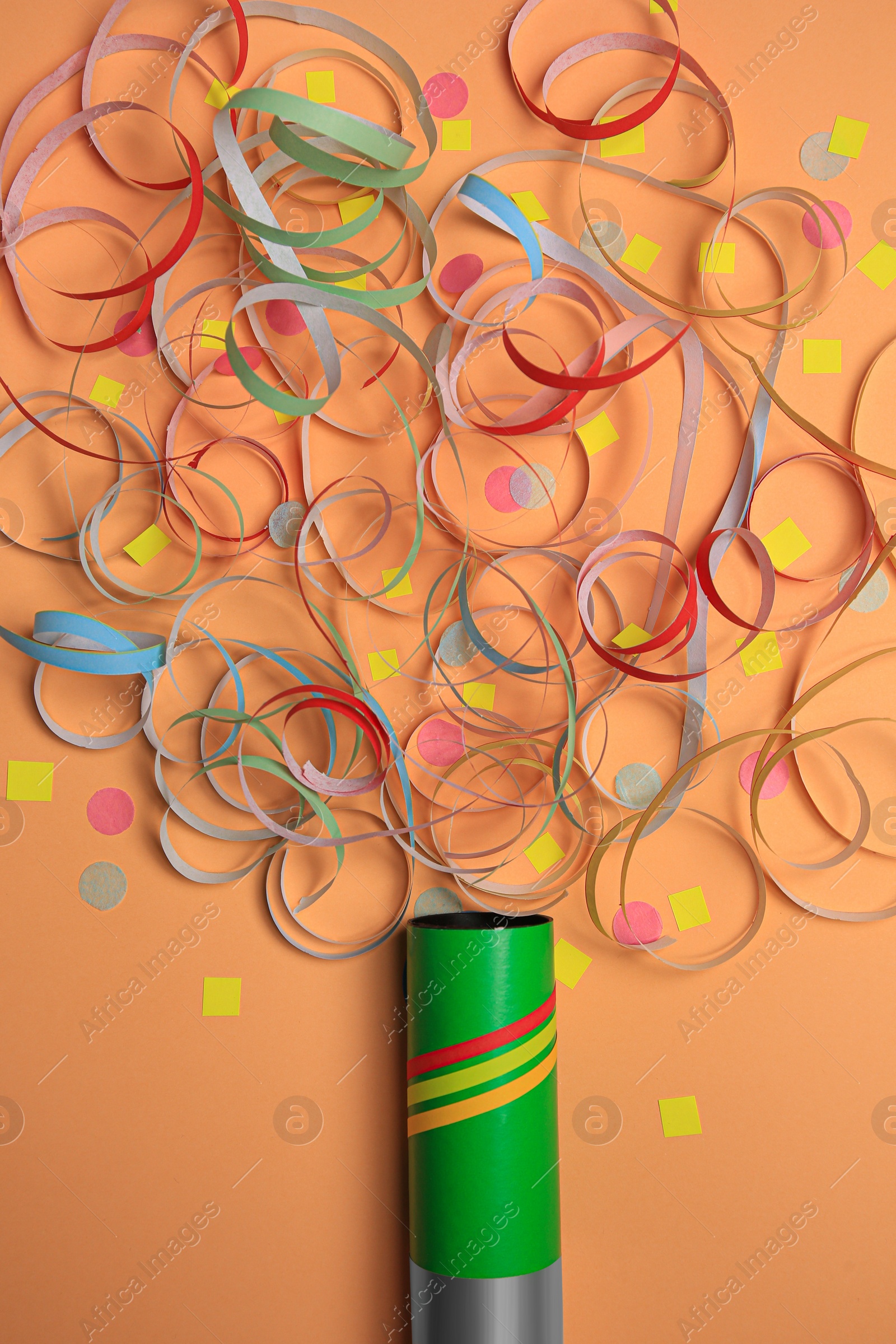 Photo of Beautiful serpentine and confetti bursting out of party popper on coral background, flat lay