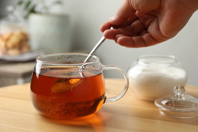 Woman stirring sugar in tea at wooden table indoors, closeup