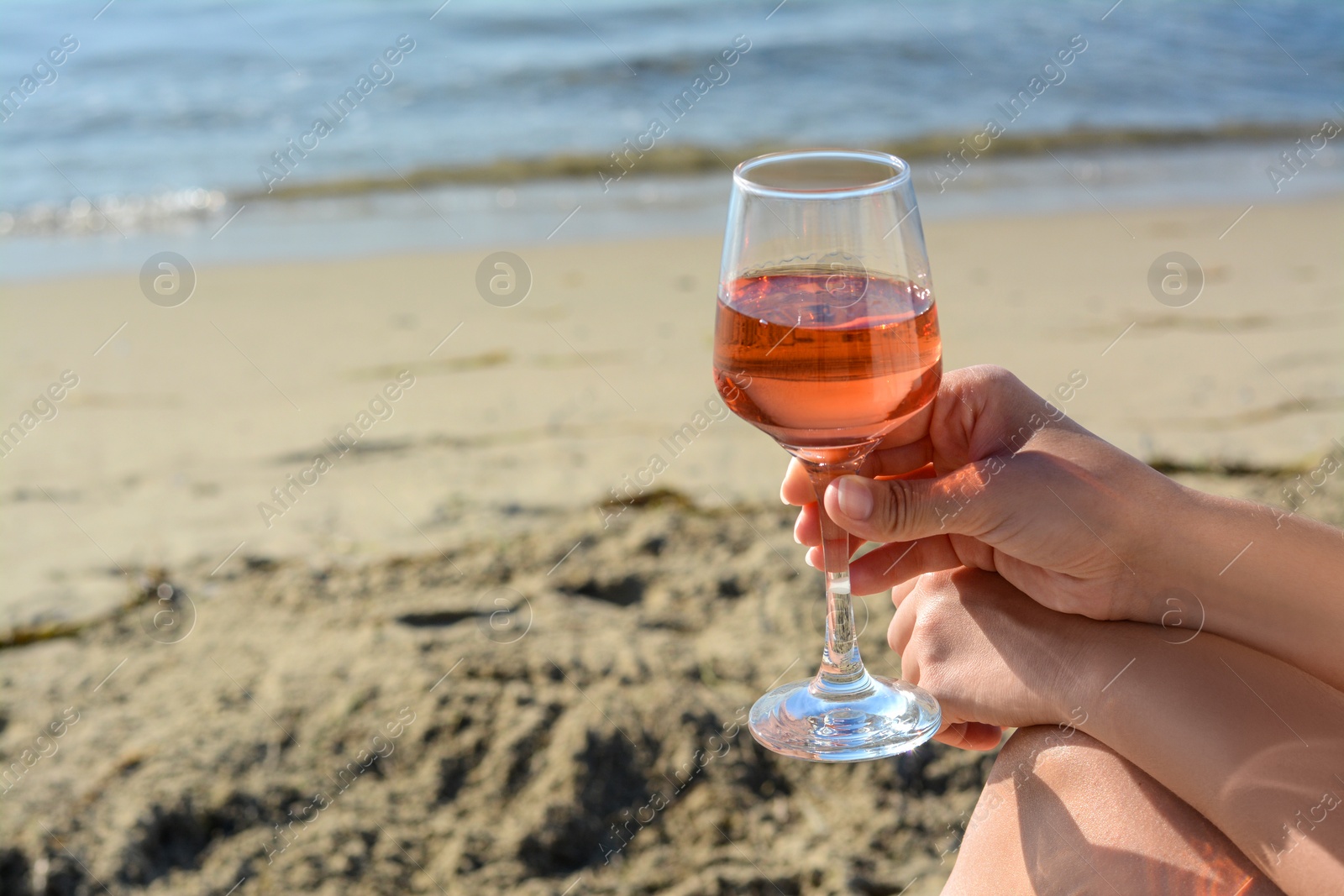 Photo of Woman with glass of tasty rose wine near sea, closeup. Space for text