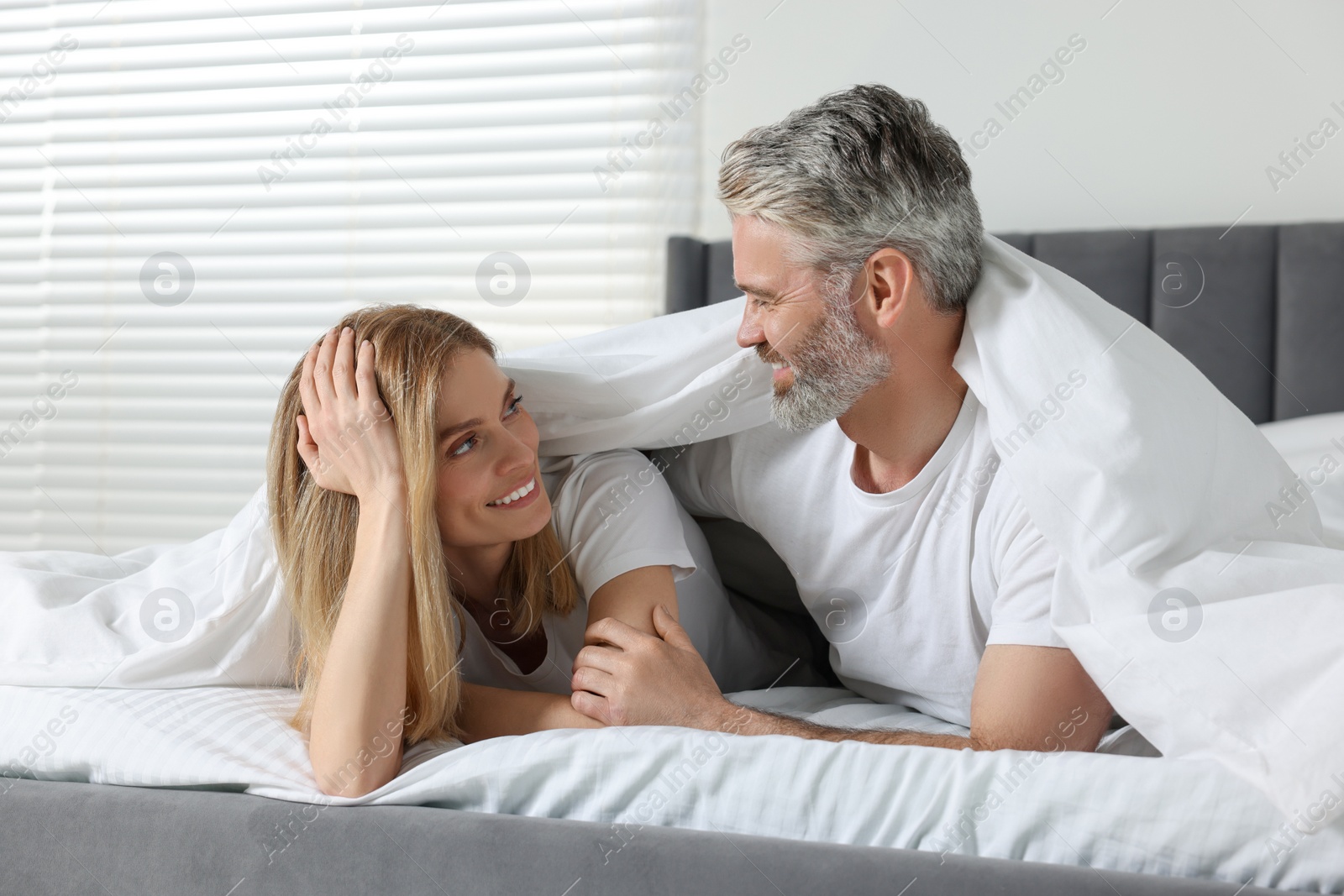 Photo of Lovely mature couple wrapped in blanket on bed at home