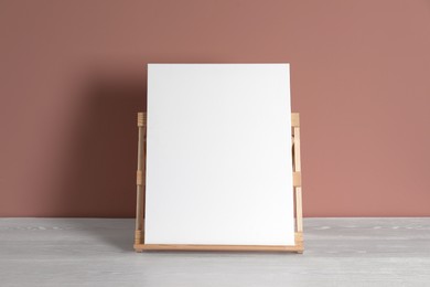 Photo of Wooden easel with blank canvas on white table