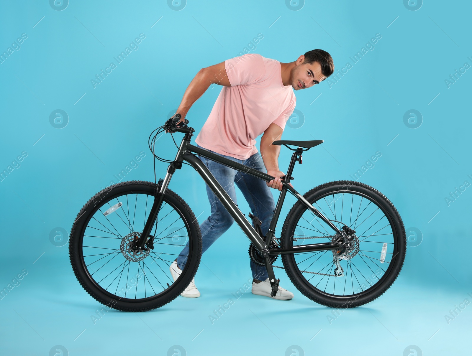 Photo of Handsome young man with modern bicycle on light blue background