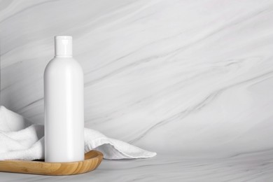 Photo of Shampoo bottle and towel on white marble table, space for text