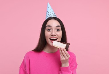 Photo of Woman in party hat eating piece of tasty cake on pink background