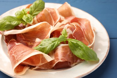 Photo of Slices of tasty cured ham and basil on blue wooden table, closeup