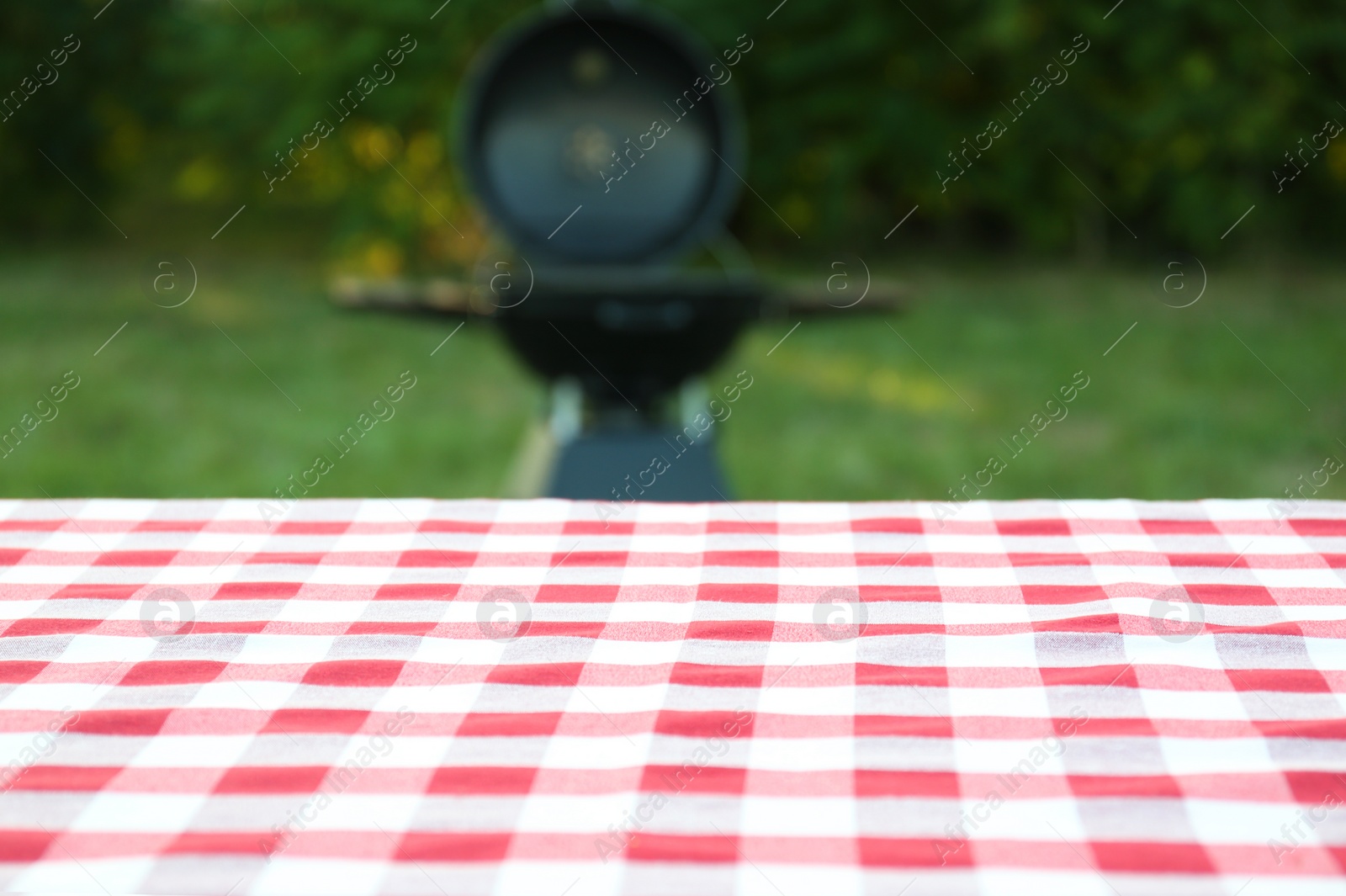 Photo of Picnic table with cloth against blurred barbecue grill outdoors