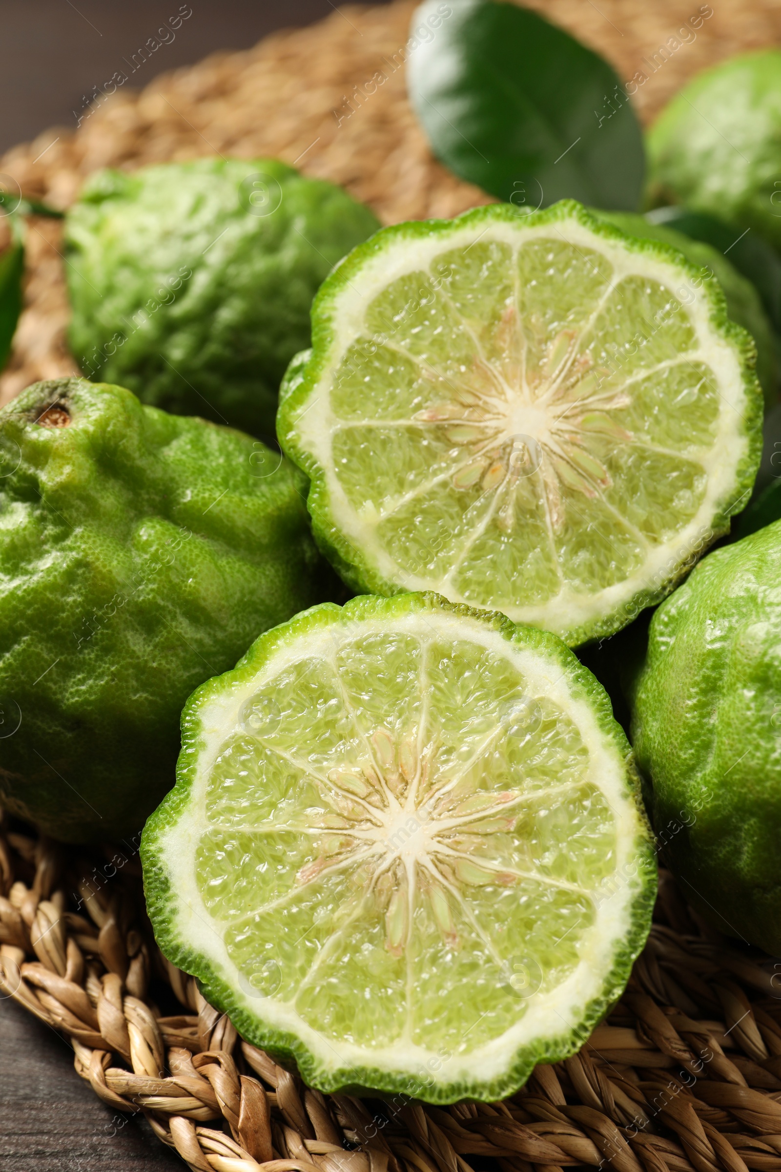 Photo of Whole and cut ripe bergamot fruits on wicker mat, closeup