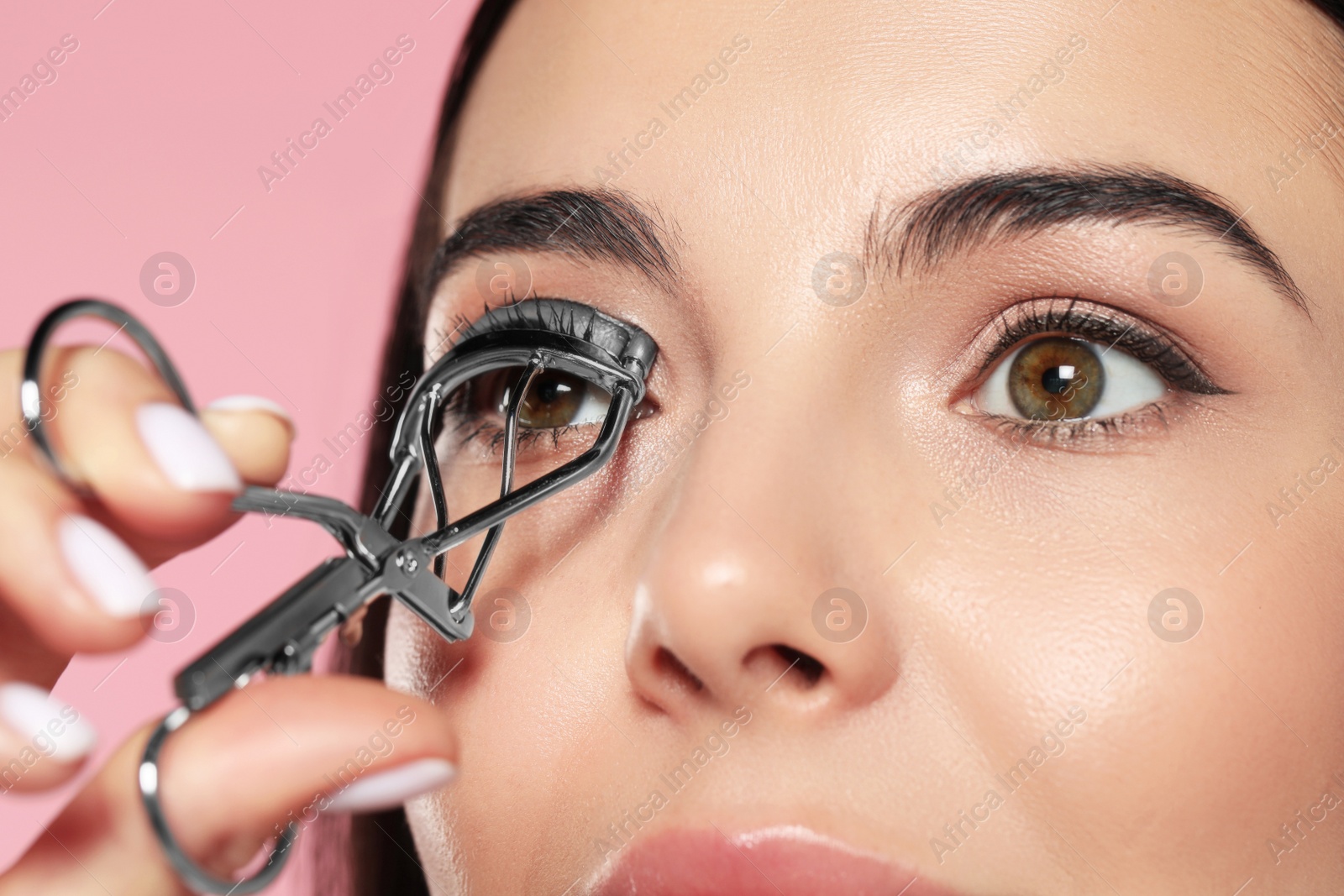 Photo of Young woman using eyelash curler on light pink background, closeup