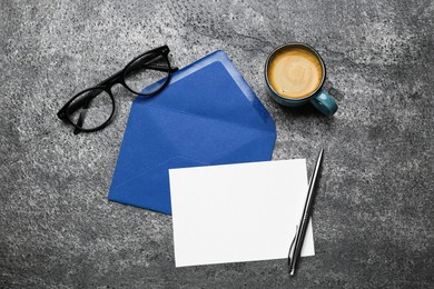 Photo of Envelope with blank paper card, cup of coffee, pen and glasses on grey table, flat lay