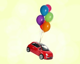 Many balloons tied to toy car flying on light yellow background