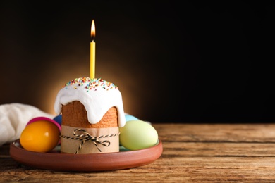 Photo of Traditional Easter cake with burning candle on wooden table against black background. Space for text
