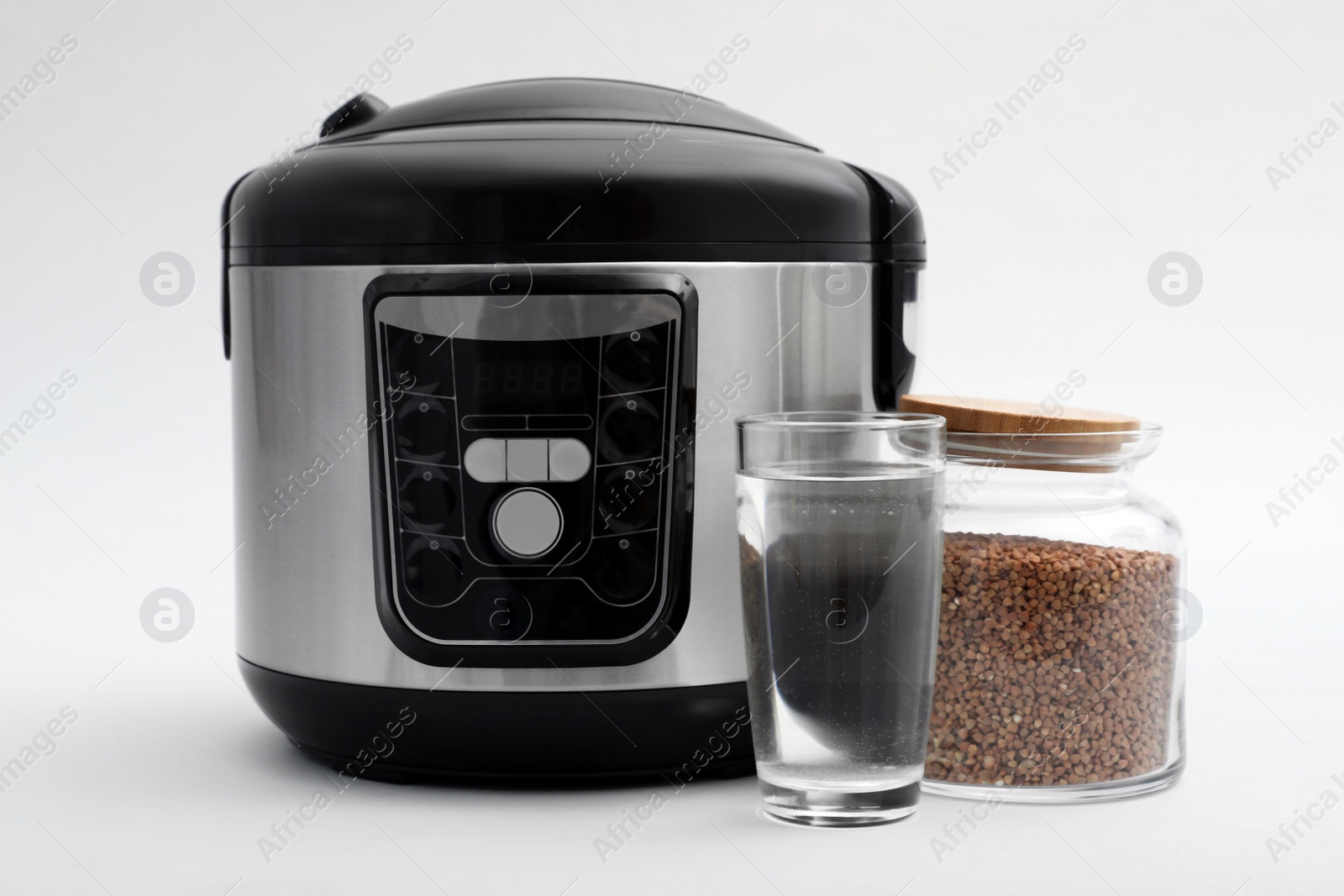 Photo of Modern electric multi cooker, buckwheat and glass of water on light background