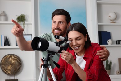 Photo of Happy couple looking at stars through telescope in room