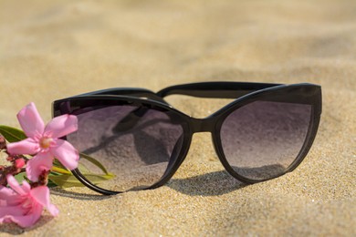 Photo of Beautiful sunglasses with flower on sand, closeup