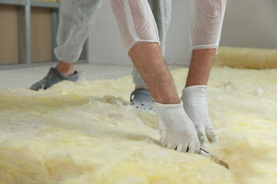 Photo of Worker cutting insulation material indoors, closeup. Space for text