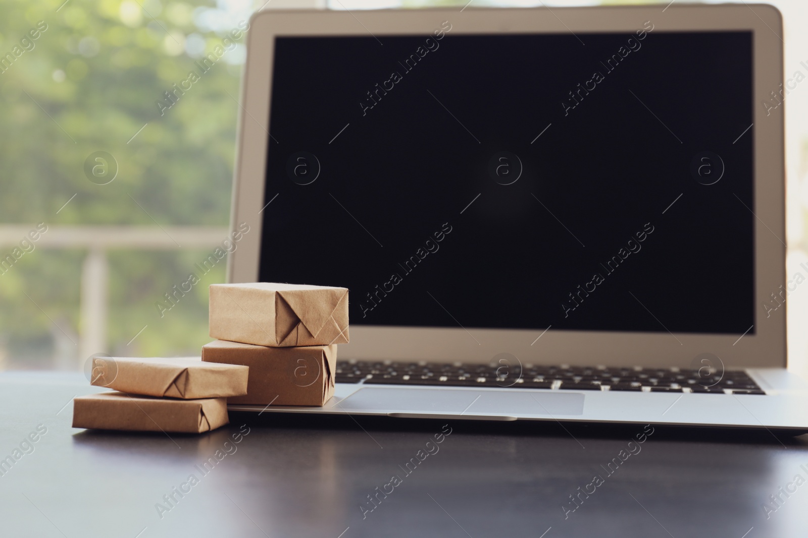 Photo of Internet shopping. Modern laptop with small boxes on table indoors