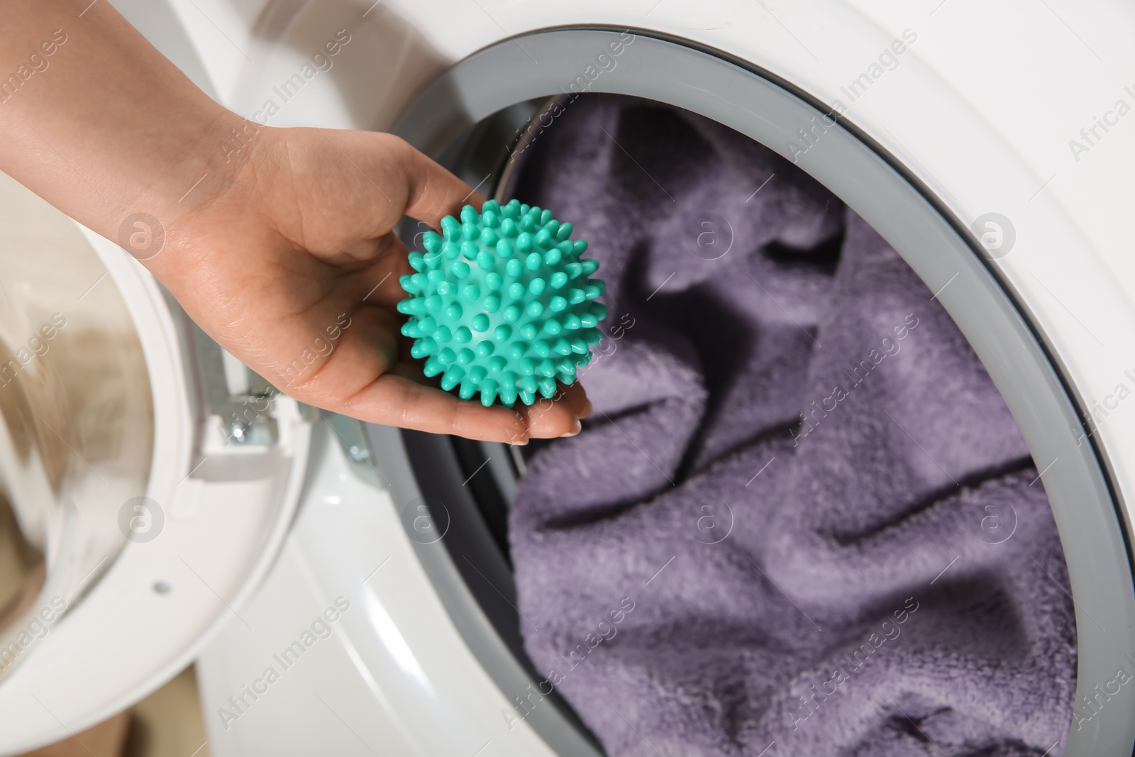 Photo of Woman putting green dryer ball into washing machine, above view