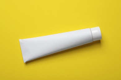 Photo of Blank tube of toothpaste on yellow background, top view