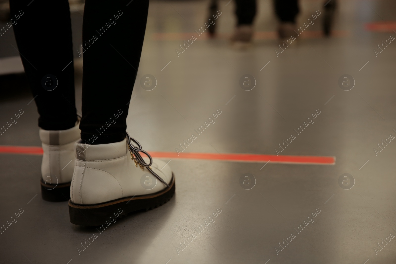 Photo of Woman standing behind taped floor marking indoors for social distance, closeup. Preventive measure during coronavirus pandemic