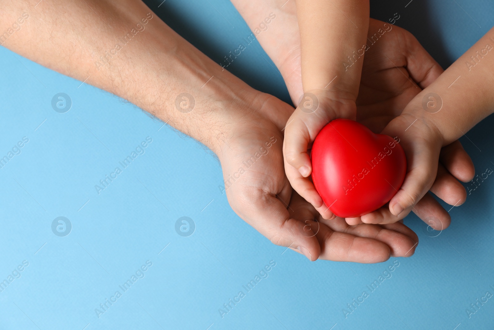 Photo of Father and his child holding red decorative heart on light blue background, top view. Space for text