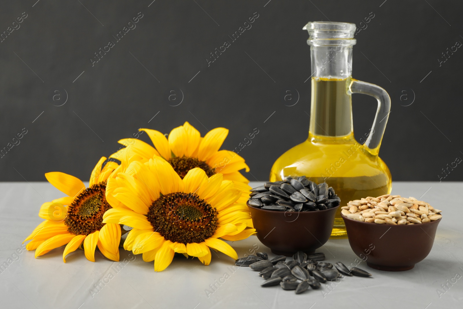 Photo of Sunflowers, jug of oil and seeds on grey table