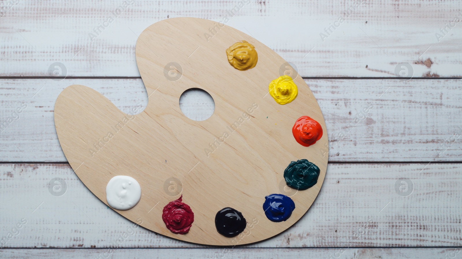 Photo of Artist's palette with samples of colorful paints on white wooden table, top view. Space for text