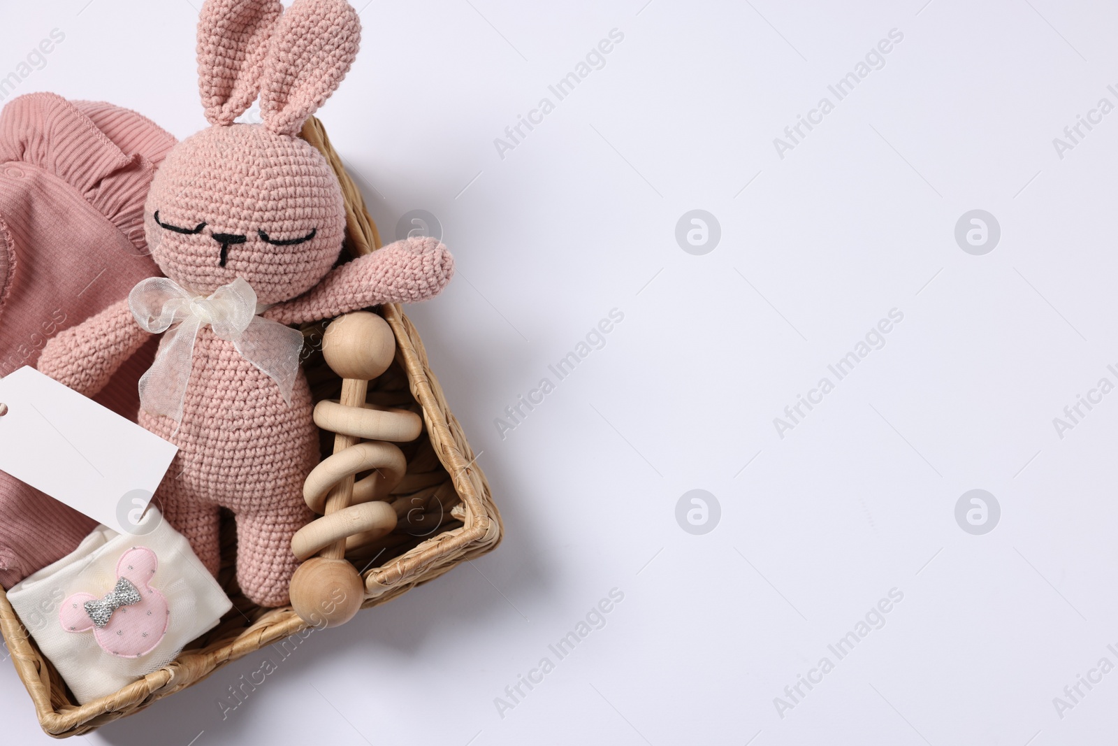 Photo of Different baby accessories, clothes and blank card in wicker box on white background, top view. Space for text