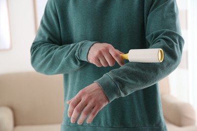 Photo of Man cleaning green sweatshirt with lint roller indoors, closeup