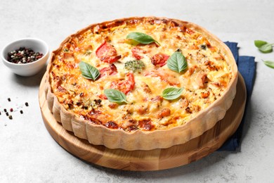 Tasty quiche with cheese, tomatoes and basil leaves on light grey table