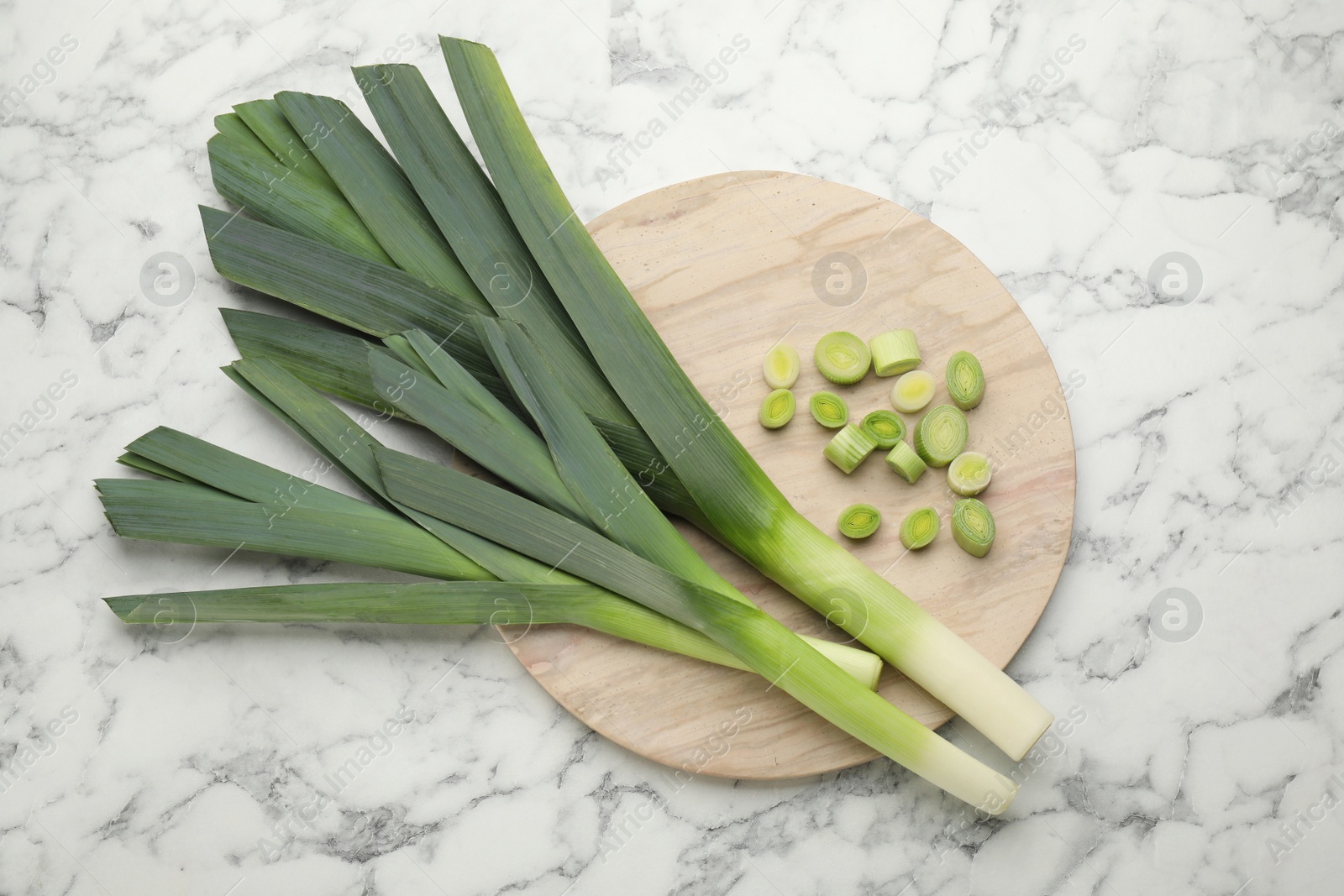 Photo of Whole and cut fresh leeks on white marble table, top view
