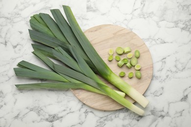 Whole and cut fresh leeks on white marble table, top view