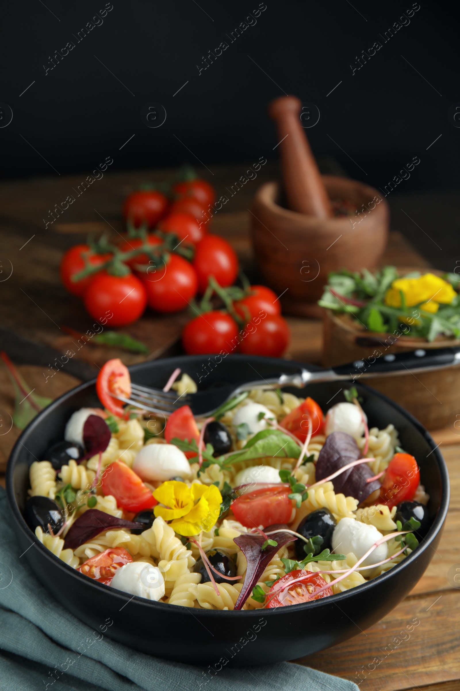 Photo of Bowl of delicious pasta with tomatoes, olives and mozzarella on wooden table