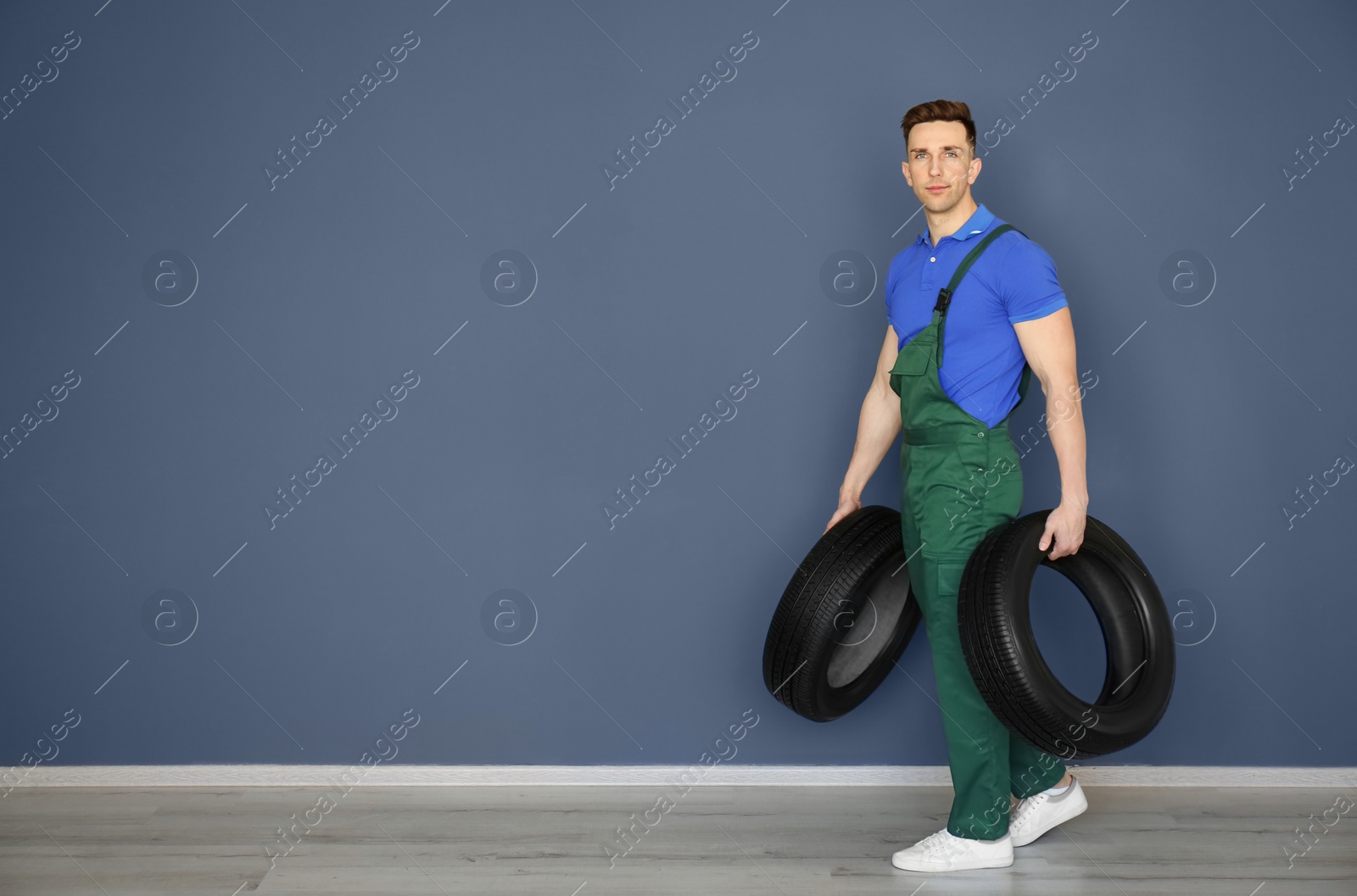 Photo of Male mechanic with car tires on grey wall background