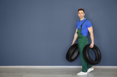 Male mechanic with car tires on grey wall background